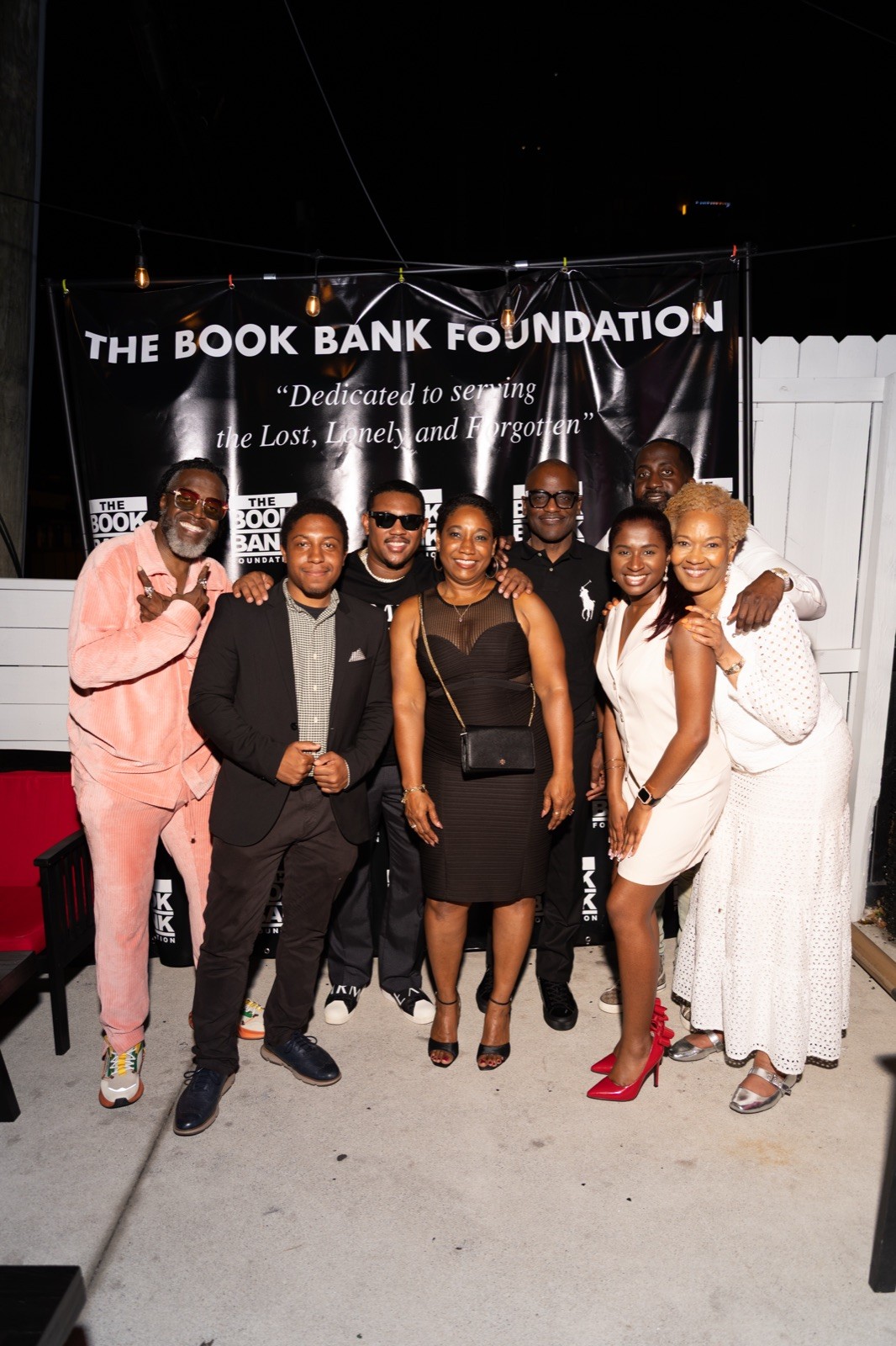Community leaders and supporters gather at an evening event beneath a Book Bank Foundation banner reading Dedicated to serving the Lost, Lonely and Forgotten.